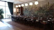 A room with a long dining table set for a meal and a mural featuring trees and flowers