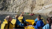Guests in life jackets floating on a raft along a river with steep rock cliffs