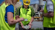 A guide and 2 Guests wearing safety gear and helmets looking at a piece of rock
