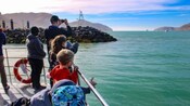 Guests standing at the edge of a boat looking out toward the water and coastline ahead