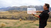 A guide holding up a still image of the town of Edoras from The Lord of the Rings next to its real world filming location