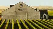 A rendering of the Abbey Winery and Brewery, featuring rows of grapevines and a large building with the winery's name and logo