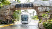 Un entorno tropical con un autobús que pasa por debajo de un puente rebosante de agua