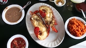 2 halves of a cooked lobster surrounded by bowls of salsa, rice and beans