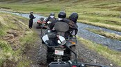 An all terrain vehicle tour guide stands near riders beside a mountain stream