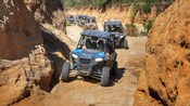 A caravan of all terrain vehicles driving on a dirt trail through desert terrain