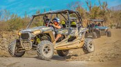 A caravan of all terrain vehicles driving on a dirt trail through desert terrain