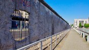 A hole in the remains of the Berlin Wall beside a walkway