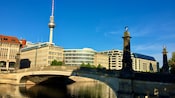 Uma ponte sobre uma via navegável em Berlim com construções urbanas e uma torre de observação