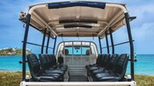 The rear of an open air truck with seats on the back parked on grass in front of water in Saint Johns, Antigua