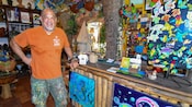 Un hombre frente a un mostrador cubierto de obras arte en la Galería de Arte Zemi en Saint John, Antigua