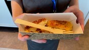 A person holding a paper basket of fried fish