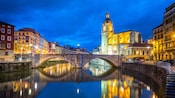 The Nervión river at night with a small arch bridge in Bilbao, Spain