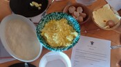 A hand holding cooked rice over bowls of rice, eggshells and cheese