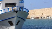 A boat sailing on the Mediterranean Sea alongside a sea wall in Chania, Greece