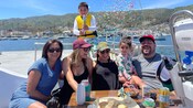 A smiling family sharing snacks on a sailboat while a boy pops a confetti cannon