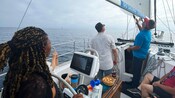 A Guest helming a sailboat while a guide shows other Guests the boom and the mainsail
