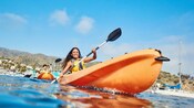 Two people kayaking near a group of boats at a harbor