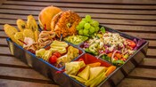 A tray filled with a gourmet lunch spread including meats, cheeses, salad and bread