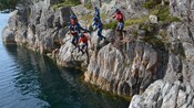 People in helmets and life jackets jump from rocks into the water
