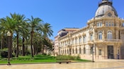 The city hall building across the street from some palm trees and grass