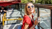 A woman in sunglasses smiling while riding on an open air bus in Rome, Italy
