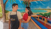 A visitor helps her companion tie his apron around his waist