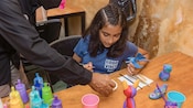 A young girl paints a wood carving of a mythical creature