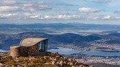A curvilinear building on a cliff overlooking a city with a river running through it