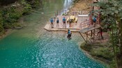 A man jumping into a swimming hole from a platform as others look on