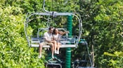 A couple sitting in an open gondola gliding through a forest