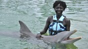 A woman petting a dolphin in the water of a pool in Grand Cayman