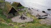 Un grupo de cabañas rústicas con techos de tepes, junto a una costa rocosa