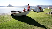 2 children sitting in a small wooden boat beached on a grassy shore