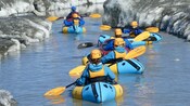 A group of Guests paddling packrafts through an icy channel by a glacier