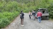 A group of people standing on a dirt road next to a UTV