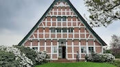 2 people in front of a building in Hamburg’s Altes Land surrounded by blooming bushes