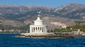 A round marble lighthouse overlooking the water and surrounded by mountains