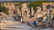People walking down a stone road lined with the ruins of an ancient city