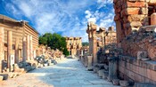 An empty street in the ruins of an ancient city is lined with crumbling building facades