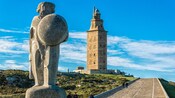 A stone statue on a hill in front of the Torre de Hércules in La Coruña, Spain