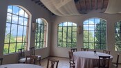 A dining room with round dining tables and windows showing the Tuscan countryside in the distance