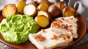 Um prato de batatas assadas, purê de batatas verdes e dois pedaços de lutefisk com bacon