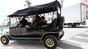 A couple being driven on a tour in a vintage wagon style car