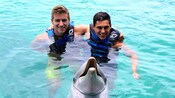 2 Guests in the Caribbean Sea with a dolphin posing for a photo