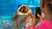 A mother photographing her 2 smiling children as they hold up a set of shark jaws