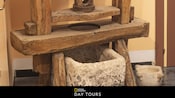 Una histórica herramienta de prensa y un receptáculo hecho de madera y piedra, con un texto debajo que dice “National Geographic Day Tours”