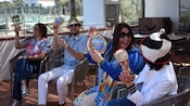 Four people seated outdoors, smiling and playing tambourines and other percussion instruments