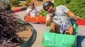 Un hombre y una mujer con cascos sonríen mientras maniobran cuesta abajo en un trineo de luge