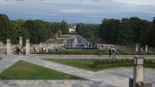 People walking around a palatial garden with a large fountain at its center